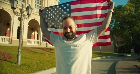 Portrait of a happy brunette guy with a beard who holds the USA flag in his Stock Footage 280571890