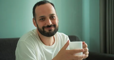 Portrait of a happy brunette guy with a beard in a white T-shirt who holds a hot Stock Footage 280668948