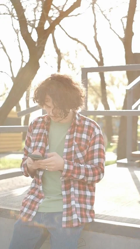 Portrait of happy curly guy typing a social media message on smartphone outdoors Stock Footage 277053042