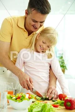 Portrait of happy father and daughter cooking vegetable salad in the kitchen Stock Photos