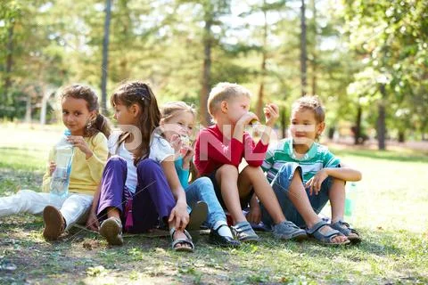 Portrait of happy friends sitting on the ground in park and having meal time Stock Photos