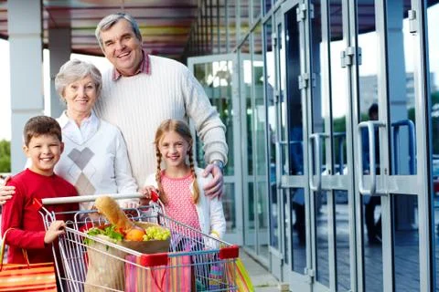 Portrait of happy grandparents and grandchildren with package of food near super Stock Photos