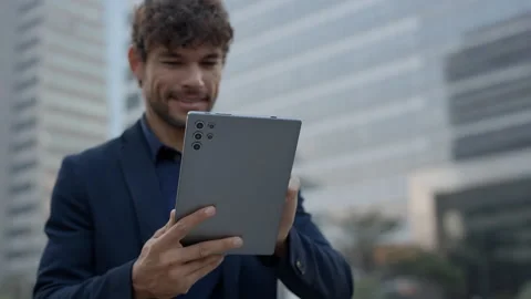 Portrait of happy Hispanic man scrolls internet on tablet in city environment Video stock 313345943