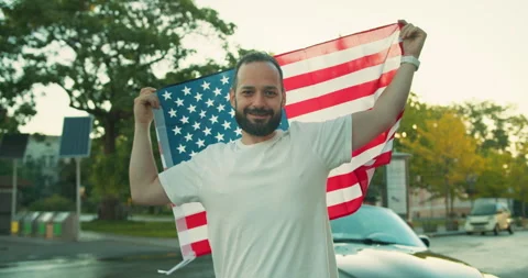 Portrait of a happy man with a beard in a white T-shirt who holds and waves a US Stock Footage 280595878