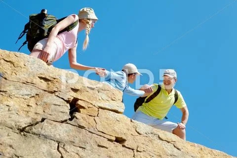 Portrait of happy man helping his wife and son to climb onto high rock Stock Photos
