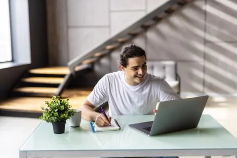 Portrait of a happy man taking notes at home look at laptop Stock Photos