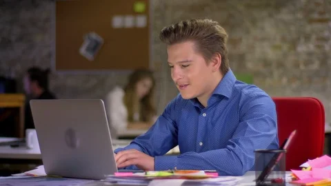 Portrait of happy middle-aged blond businessman in front of laptop achieving Video stock 99709574