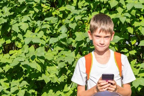 Portrait of a happy schoolboy with a backpack using a smartphone, writing onl Stock Photos