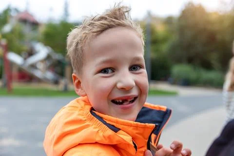 Portrait happy smiling boy with missing tooth wearing bright orange jacket at Stock Photos