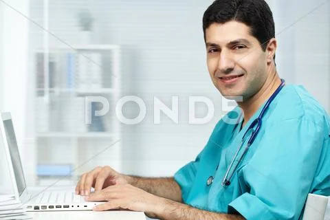 Portrait of happy surgeon typing on laptop and looking at camera Stock Photos