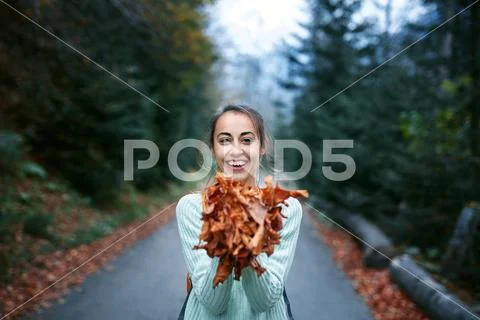 Portrait of a happy woman playing with autumn leaves in forest Stock Photos