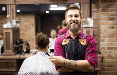 Portrait of happy young barber with client at barbershop and smiling. Stock Photos