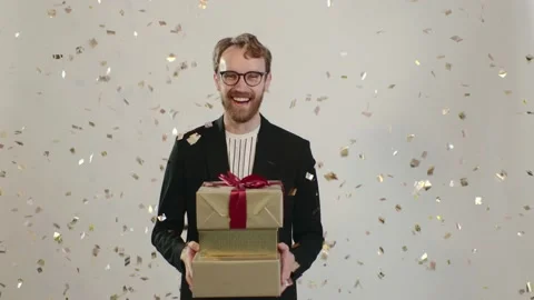 Portrait of a happy young man with a big smile holding gifts as golden confetti. Stock Footage 221642853