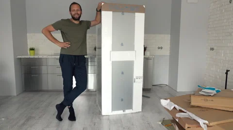 Portrait of happy, young man fitting new fridge to furniture at his new home Stock Footage 67508336