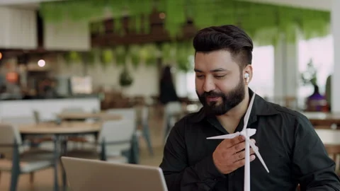 Portrait of Indian engineer turns mini windmill propeller model at video call Stock Footage 319630977