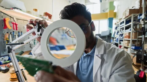 Portrait of Indian Man Examining Circuit Board through Magnifying Glass Stock Footage 343510699