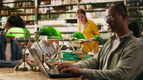 Portrait of indian smiling tutor looking up from laptop screen at library desk Stock Footage 336359146
