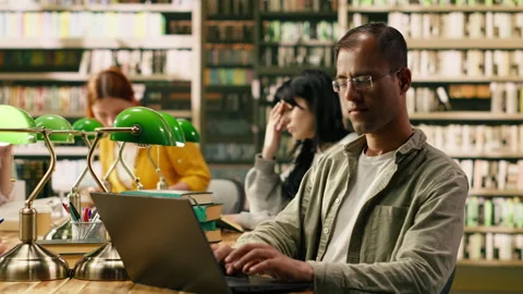 Portrait of indian smiling tutor looking up from laptop screen at library desk Stock Footage 336361094