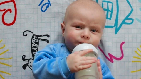 Portrait of infant baby tries to eat from a bottle in bed by himself. Healthy Stock Footage