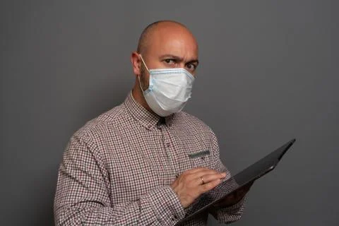 Portrait of a keep working bearded man with tablet in hands in a gauze mask P Stock Photos