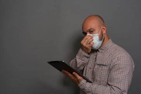 Portrait of a keep working bearded man with tablet in hands in a gauze mask P Stock Photos