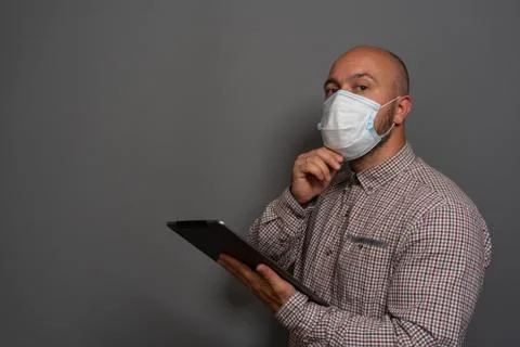 Portrait of a keep working bearded man with tablet in hands in a gauze mask P Stock Photos