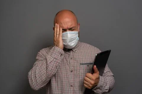 Portrait of a keep working bearded man with tablet in hands in a gauze mask P Stock Photos