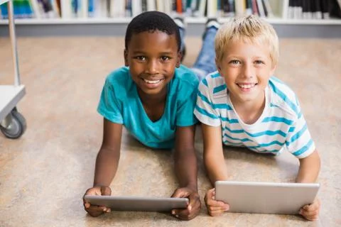 Portrait of kids lying on floor using digital tablet in library Stock Photos