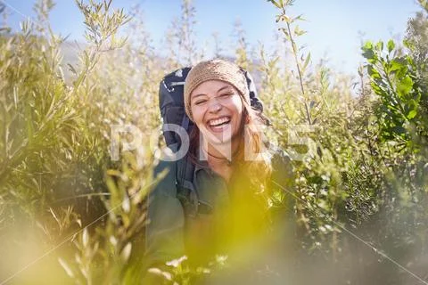 Portrait laughing young woman with backpack hiking in sunny field Stock Photos