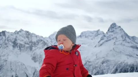 Portrait of a little boy in a red jacket against a background of snowy mountains Stock Footage 163304943