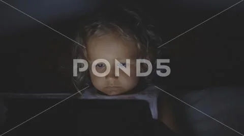 Portrait of little child girl using tablet technology in bed by night at home. Stock Photos