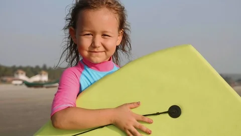 Portrait of little girl surfer with a surfboard in her hands on the beach. Stock Footage