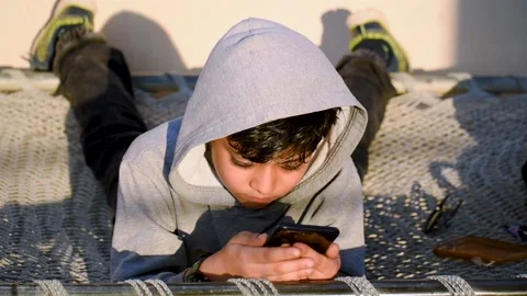 Portrait of little Indian kid using a mobile phone while chilling on the bed. 스톡 동영상 144692377