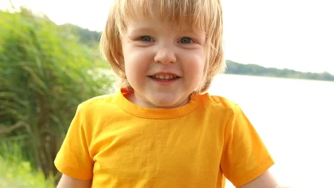 Portrait of little thoughtful blonde boy resting near the forest summer lake. Видео 113686932
