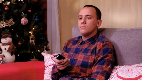 Portrait of a lonely man sitting on sofa near the christmas tree and watching tv Video stock 124977355