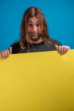 Portrait of long haired man making a funny face while holding a blue advertise Stock-Fotos