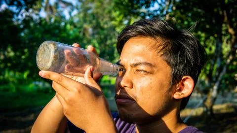 Portrait of Malay man seeing inside a glass bottle which act as binocular. Stock Photos