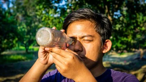 Portrait of Malay man seeing inside a glass bottle which act as binocular. Stock Photos