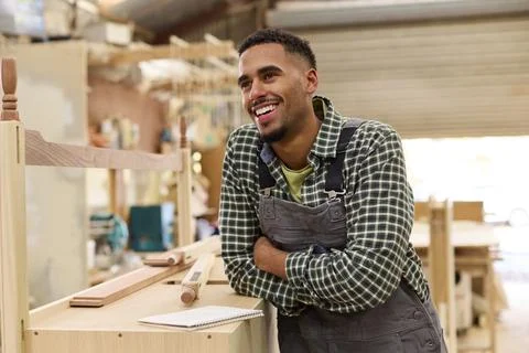 Portrait Of Male Apprentice Working As Carpenter In Furniture Workshop 库存照片
