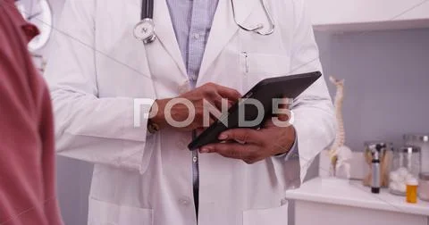 Portrait Of Male Black Doctor Using Tablet Device With An Elderly Patient
