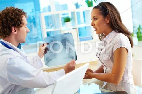 Portrait of male doctor showing young female patient x-ray in hospital Stock Photos