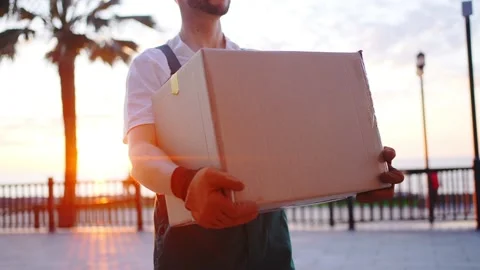 Portrait of a male loader in uniform with a box in his hands at sunset close up Stock Footage 238774789