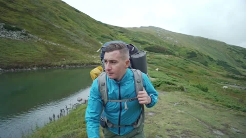 Portrait of a man with a backpack walking next to a lake in the mountains Stock Footage 236981488