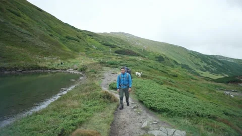 Portrait of a man with a backpack walking next to a lake in the mountains Stock Footage 236982827