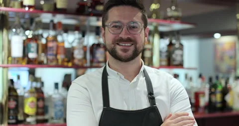Portrait of a man bartender in glasses in a black apron standing behind the bar Stock Footage 319024959