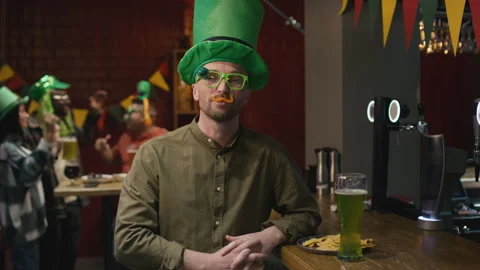 Portrait of Man in Big Green Hat and Funny Glasses Posing in Irish Pub Stock Footage 261498269