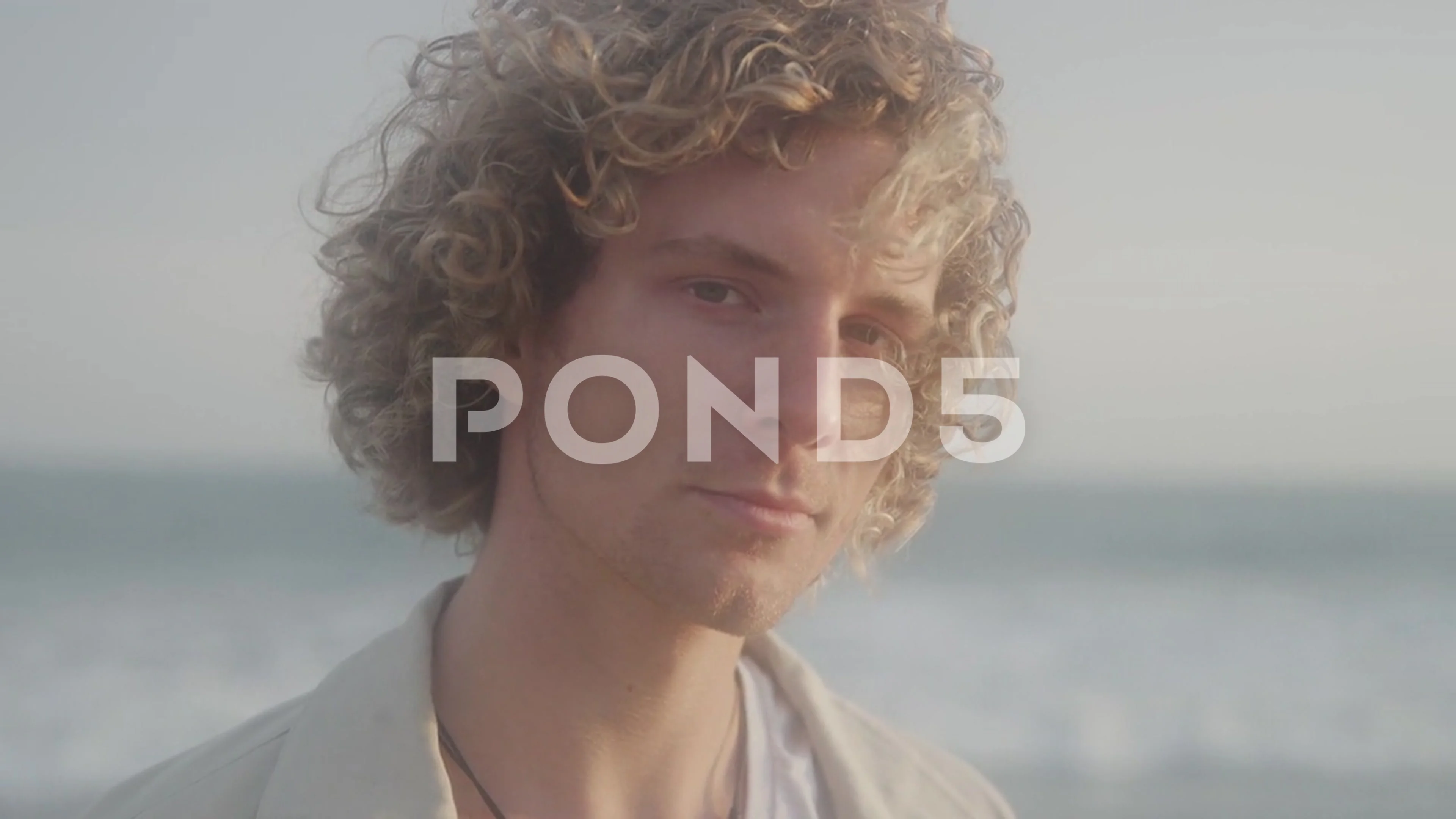 Portrait of Man with Blonde Curly Hair and Serious Expression Standing on  Beach