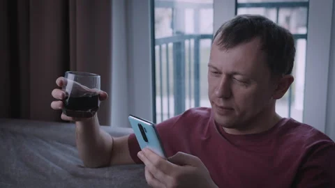 Portrait of a man browsing messages on his phone and drinking from a glass Stock-Footage 331201024