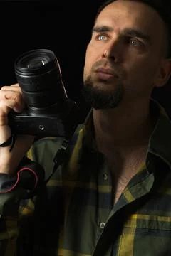 Portrait of a man with a camera. Black background. Photographer in green plai Stock Photos