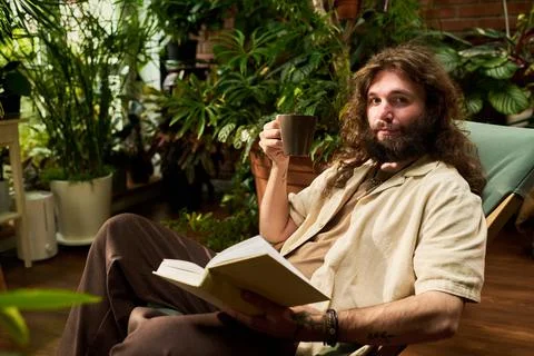 Portrait of Man Drinking Coffee and Reading Book among Houseplants Fotos de archivo